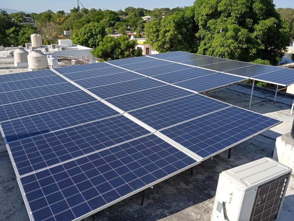 Conjunto de paneles solares en un tejado plano con árboles y edificios al fondo.