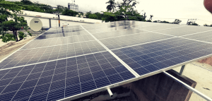 Paneles solares en un tejado con árboles y una antena parabólica al fondo.