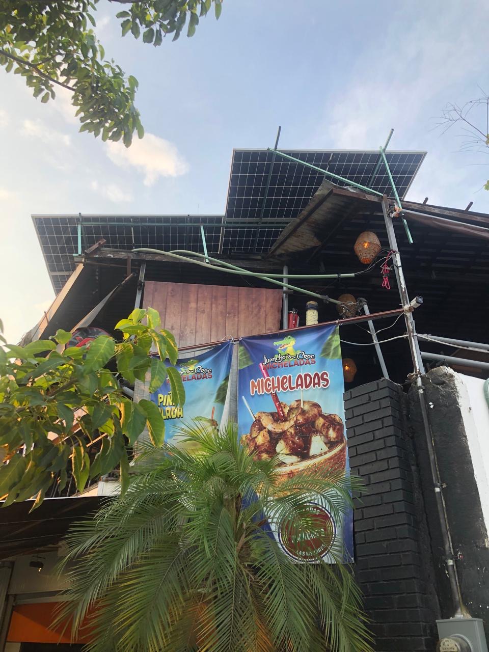 Edificio con paneles solares y anuncios de bebidas entre follaje tropical.